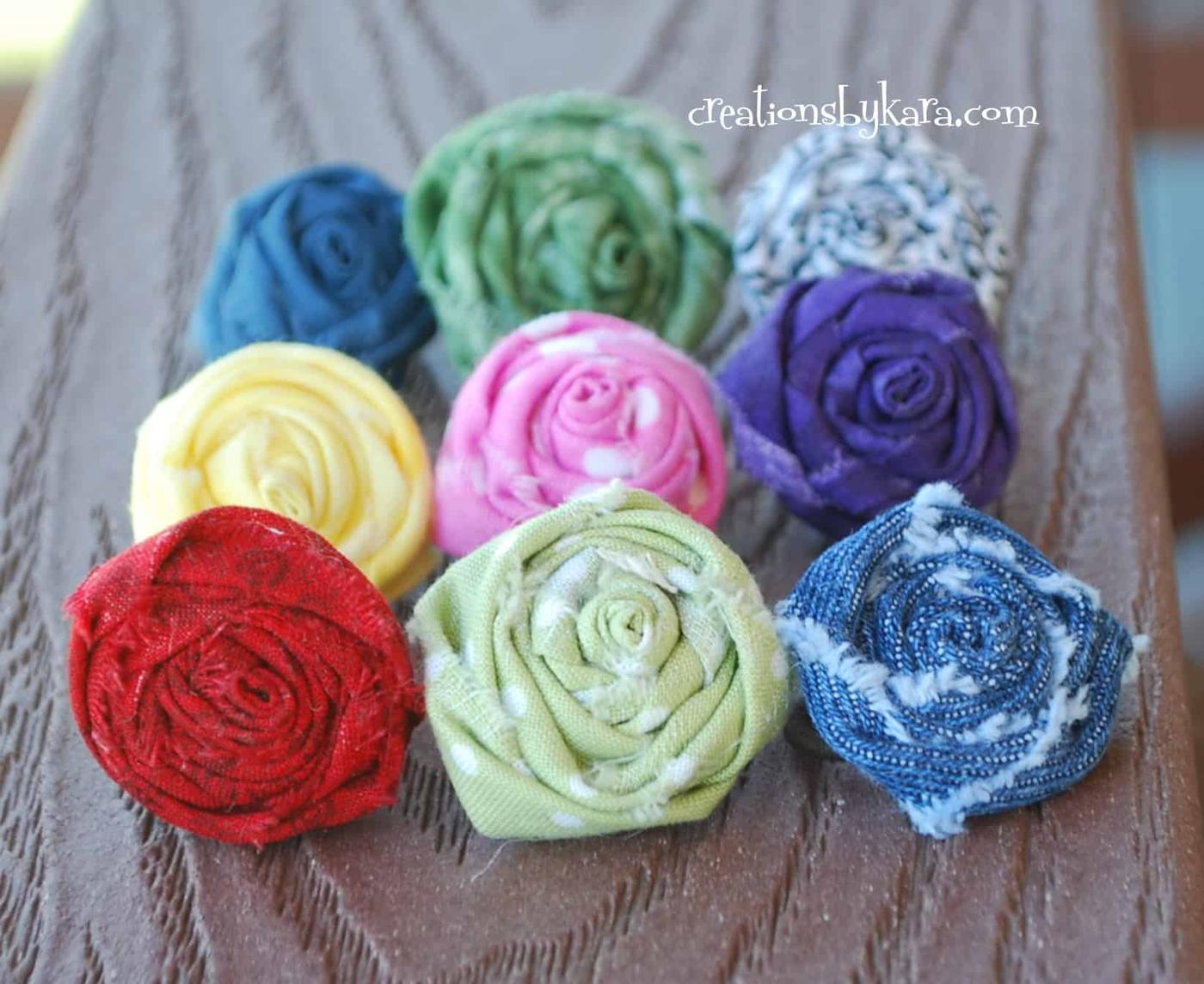 Rolled fabric rosette rings in red, pink, green, blue and purple fabrics grouped together on a wood table