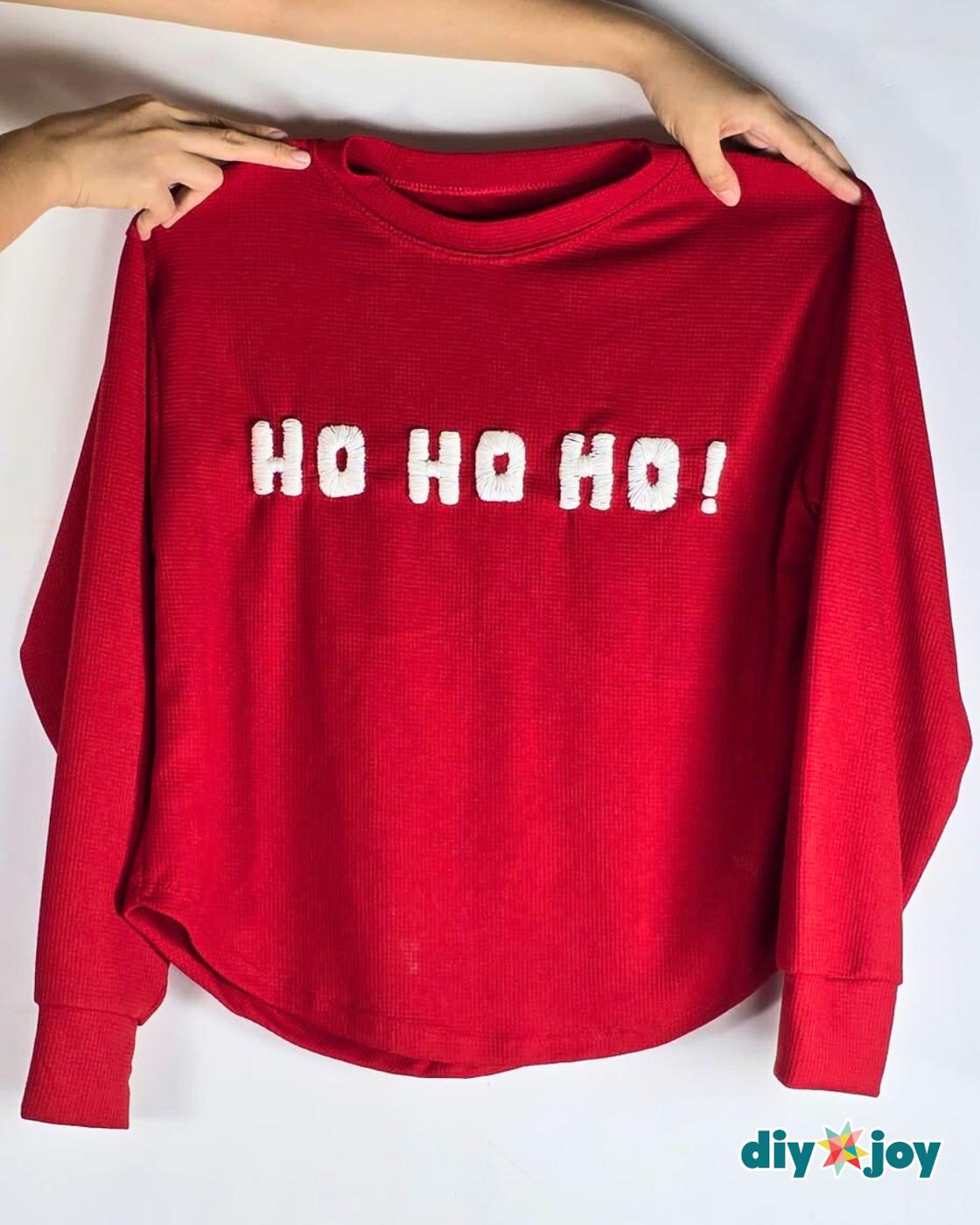 How to Make a Christmas Sweater - two hands holding the finished red sweater up by the shoulders with HO HO HO in white across the front
