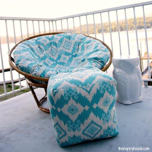 Turquoise and white ikat print pouf ottoman in outdoor fabric on a balcony beside a matching papasan chair