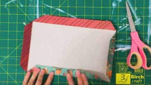 Hands pressing a DIY journal cover made from red striped and teal fox print paper on a green cutting mat with scissors