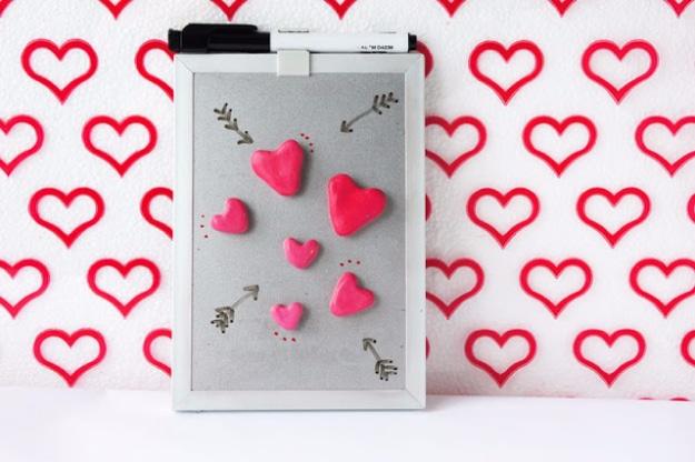 Small handmade heart magnets in pink and red arranged on a refrigerator door holding a note to make at home