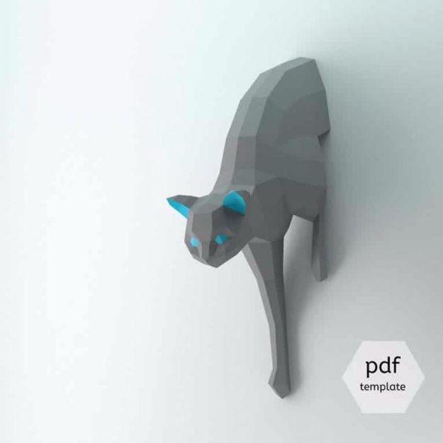 3D paper craft cat origami, a grey low poly paper cat sculpture with turquoise eyes mounted on a pale wall
