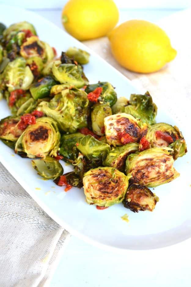 Lemon and sun-dried tomato brussels sprouts roasted golden brown and tossed in a glossy lemon sauce in a white bowl