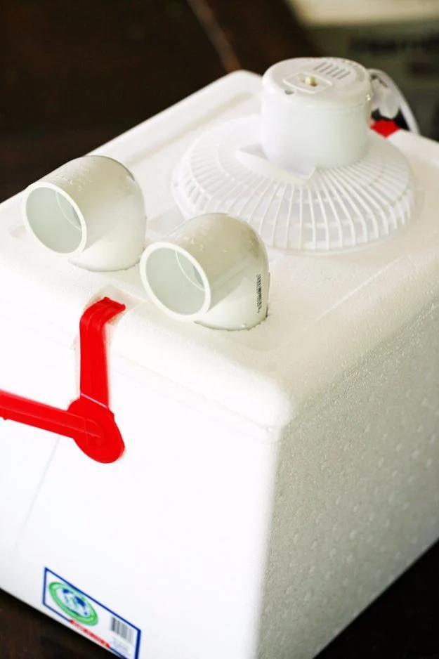 Homemade air conditioner made from a white cooler with two plastic elbow vents and a small fan on the lid