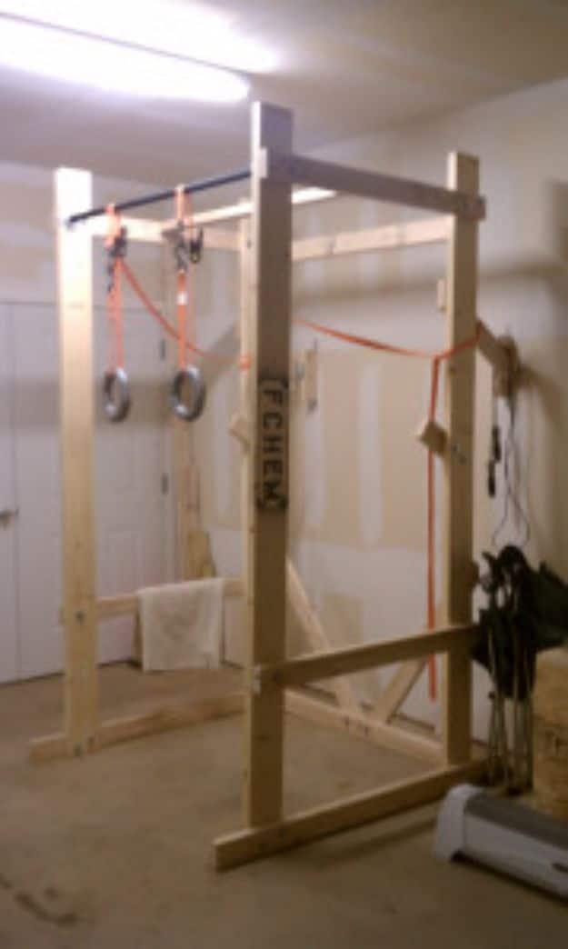 Timber power rack with a steel pull up bar, gymnastic rings and resistance bands hanging inside it in a basement