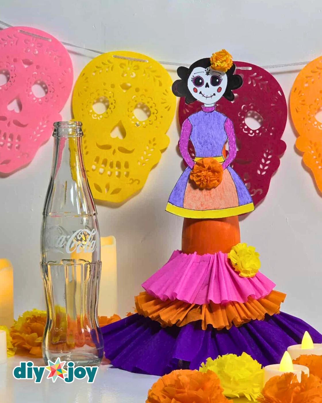 Recycled Crafts - the finished La Catrina standing beside an empty clear glass Coca-Cola bottle so you can see exactly what she started as