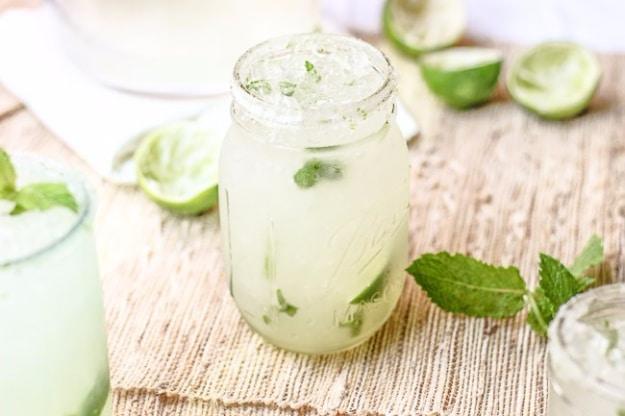 Mint limeade fizz in a jar over ice with thin lime wedges and sliced mint leaves, limes on the table