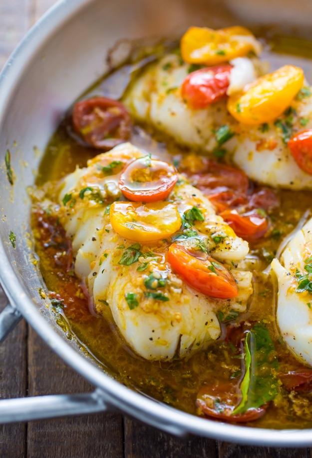 Pan seared cod fillets in a white wine tomato basil sauce with fresh basil leaves in a skillet for an easy fish dinner