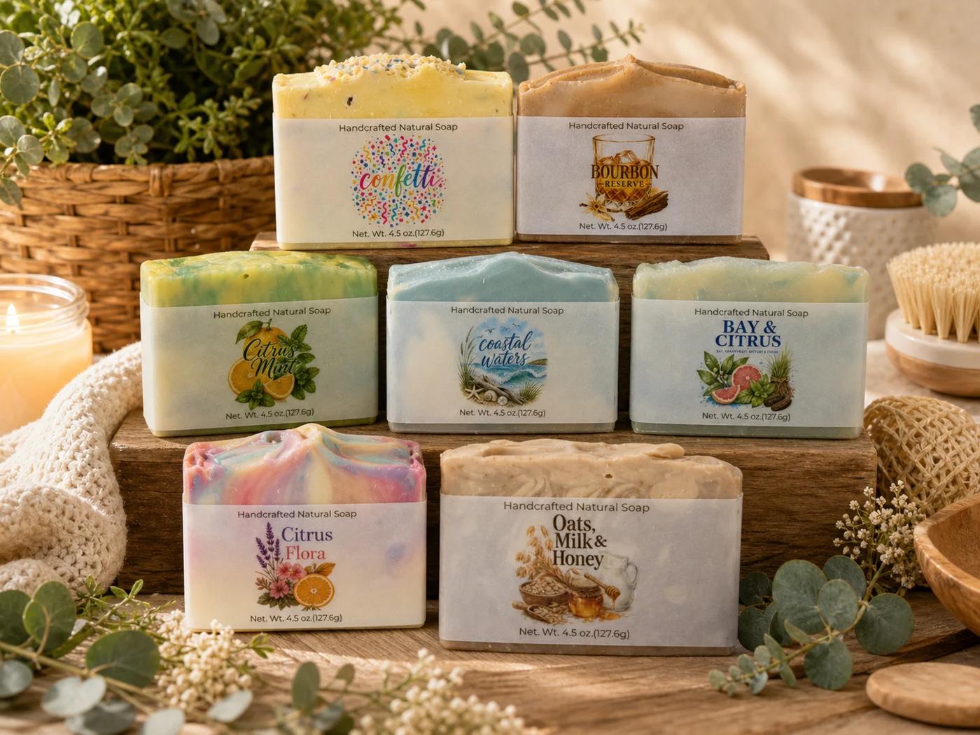 Seven bars of handmade soap in pastel swirls with printed paper labels stacked on a wood block with eucalyptus