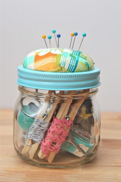 Pint mason jar of sewing supplies with a fabric pincushion built into the painted lid ring and pins stuck in it