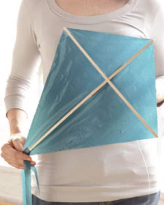 Kite made from a teal plastic bag on two crossed wooden dowels, held up against a person's body with its tail hanging