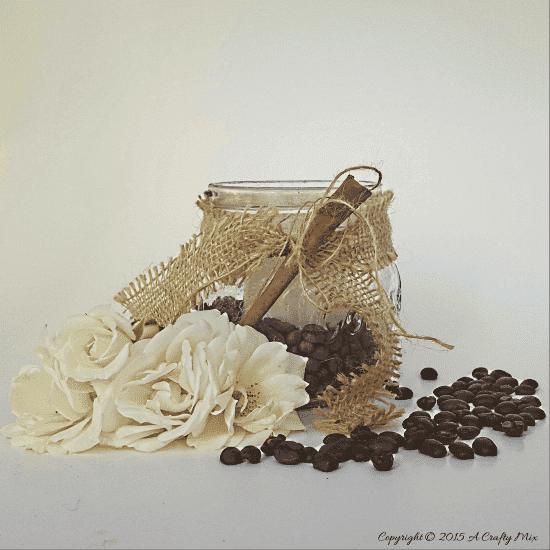Mason jar packed with coffee beans and vanilla pods around a lit white pillar candle, tied with rustic ribbon