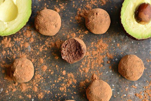 Silky dark chocolate avocado truffles rolled in cocoa on dark slate with halved avocados around the edges