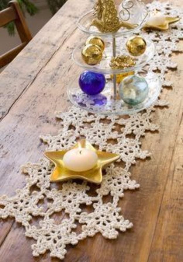 Cream crocheted snowflake table runner flecked with gold, running down a rustic wooden dining tabletop