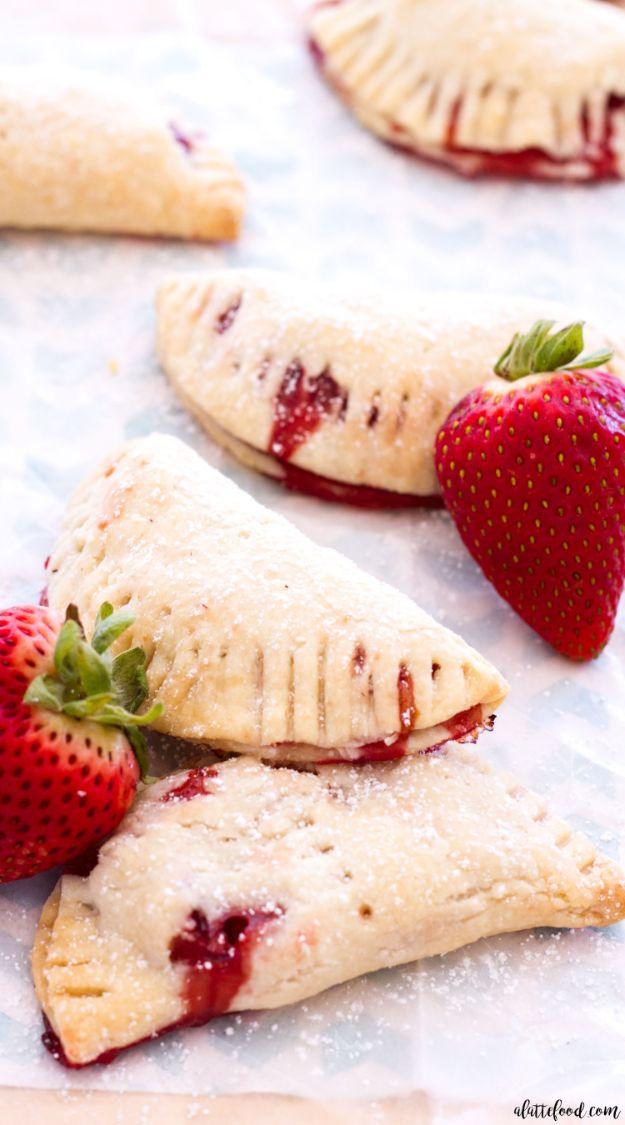 Strawberry hand pies with crimped cream cheese crust and berry filling leaking out on parchment paper