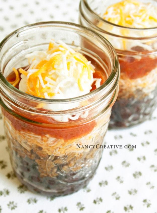 Burrito in a cup layered in a small canning jar with black beans, taco meat, cheese, salsa and sour cream