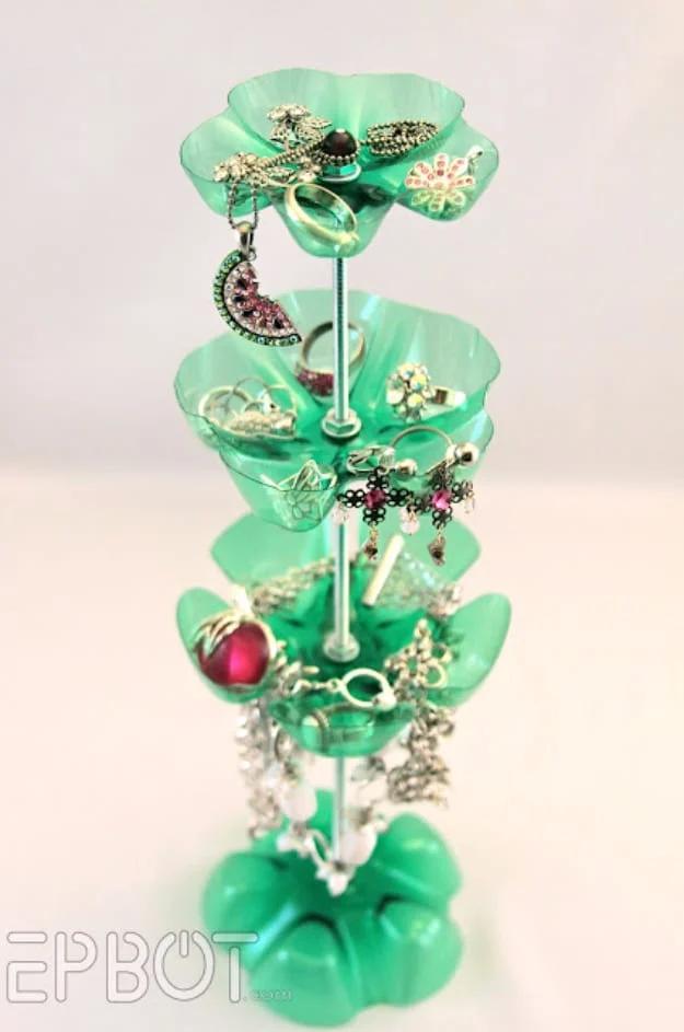 Four tier jewelry stand made from green soda bottle bottoms threaded on a metal rod, holding rings, earrings and necklaces
