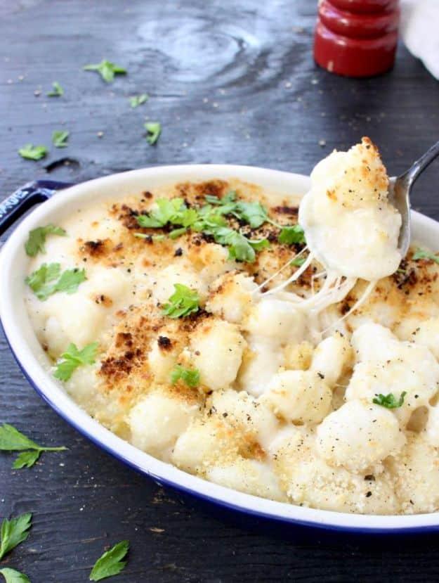 Gnocchi mac and cheese in a white enamel dish with a blue rim, browned on top, with parsley and a spoon
