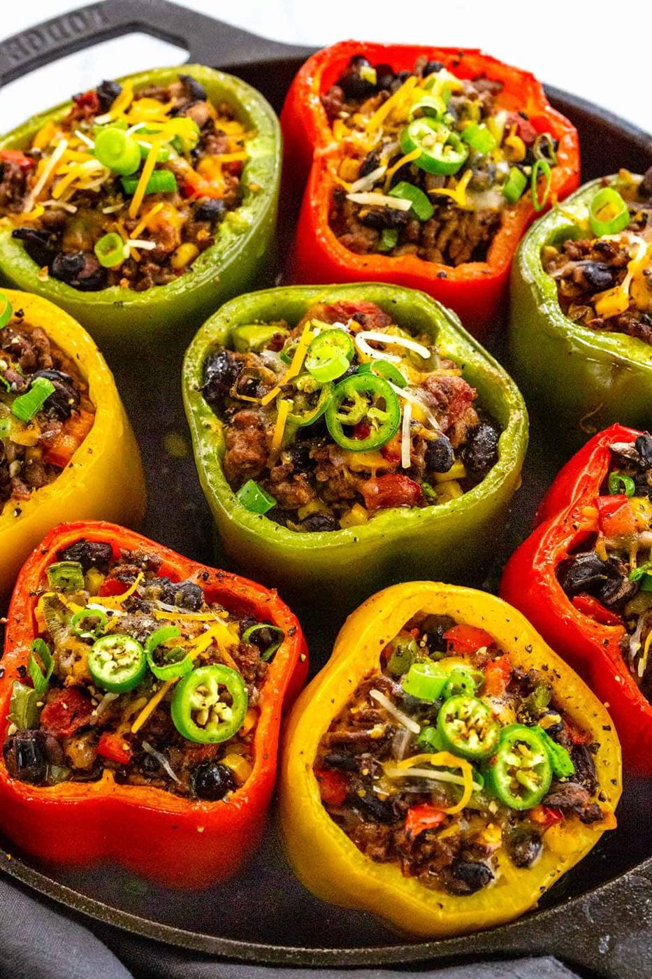 Stuffed bell peppers in red, green and yellow filled with ground beef, beans and melted cheese in a skillet
