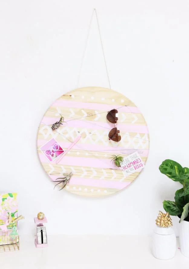 Mud cloth inspired organizer, a painted wooden circle with crisscross cords holding photos, hung on a white wall