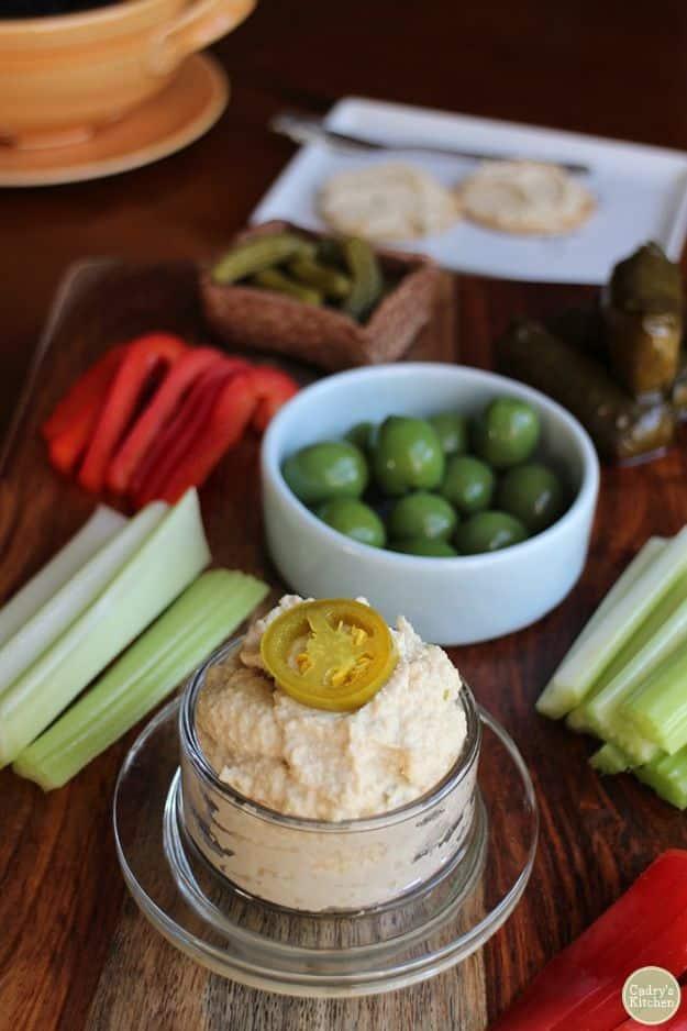 Jalapeño cashew cheese spread in a glass jar topped with a pepper slice, olives and celery beside it