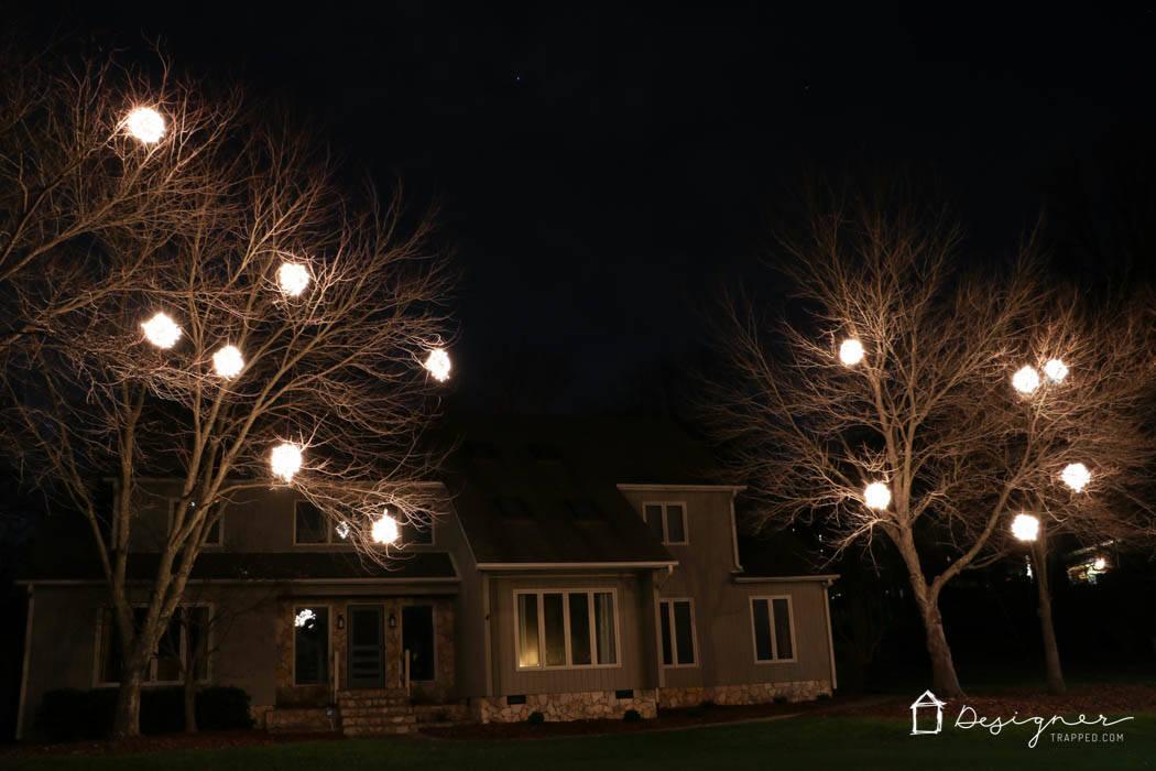 Glowing wire spheres wrapped in string lights hanging at different heights in bare winter tree branches