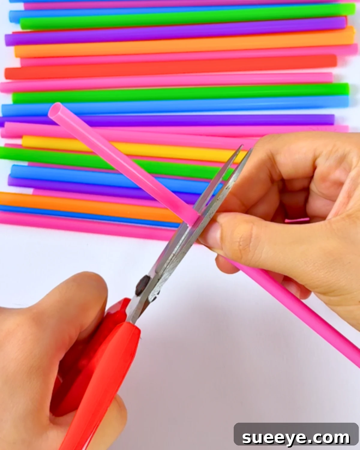 Cutting a pink cocktail straw in the middle to prepare the petals for the flower assembly.