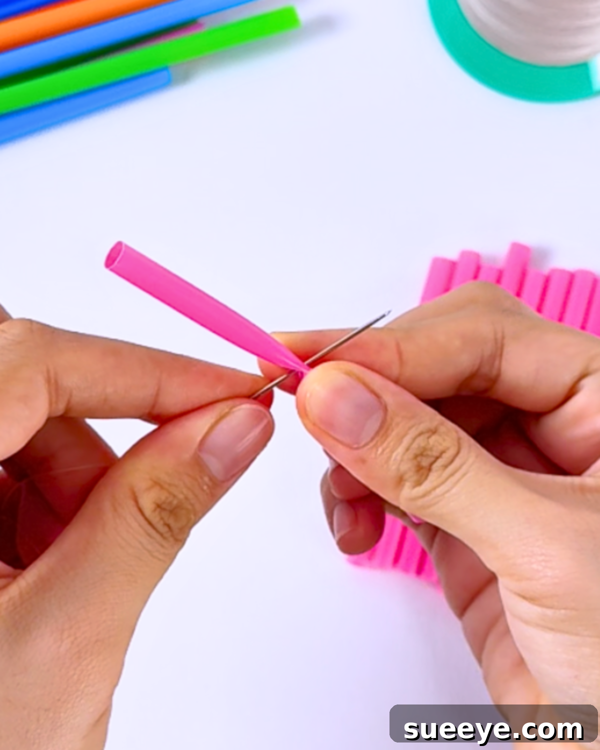 Inserting a needle into the center of a cut straw to assemble the cocktail straw flower parts together.