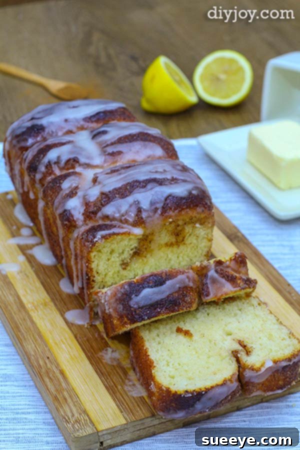 A close-up view of powdered sugar in a white bowl, a metal whisk, and a glass of milk, with a freshly baked loaf of cinnamon bread blurred in the background, preparing for the final glaze.