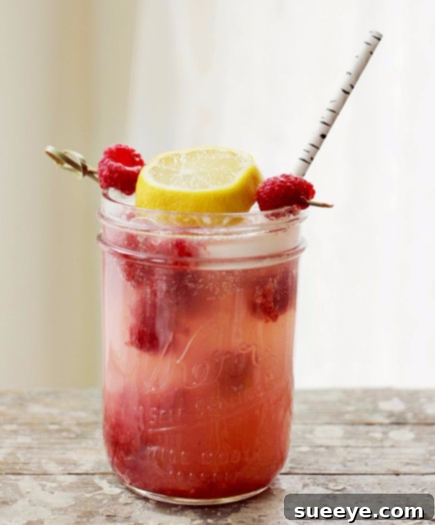 Zesty Smashed Raspberry Lemonade Cocktail Smashed Raspberry Lemonade Cocktail in a glass with fresh raspberries and lemon.