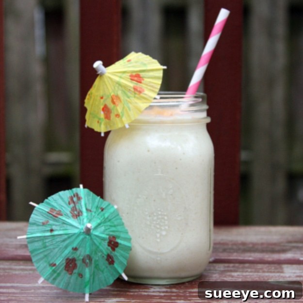 Tropical Pina Colada Breakfast Smoothie: Start Your Day with Sunshine Pina Colada Breakfast Smoothie served in a clear glass with a straw and pineapple wedge.