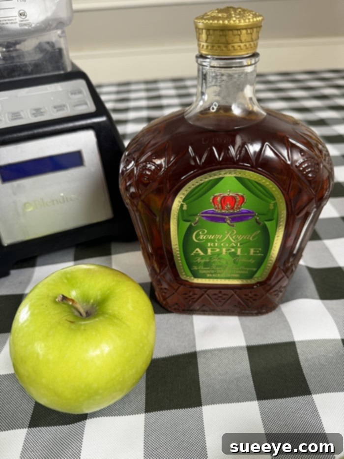 Rancher's Crown Royal Apple Slush 3 Bottle of Crown Royal Apple whisky next to a glass of green apple slushie and fresh apples