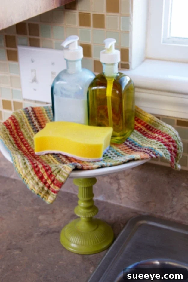 Dish Soap Cake Stand Organizer Dish soap and sponges neatly arranged on a small cake stand by the kitchen sink.