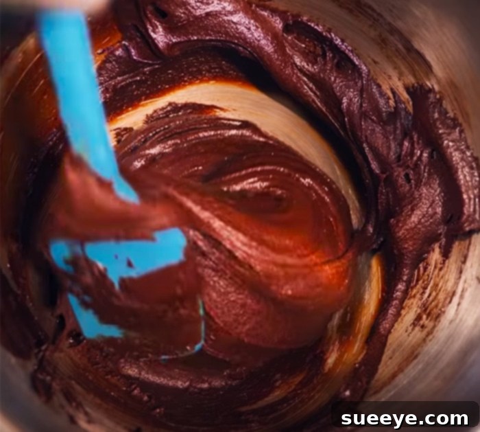 Prepare the rich chocolate brownie batter, ensuring a smooth and glossy mixture for the base of your cheesecake brownies.