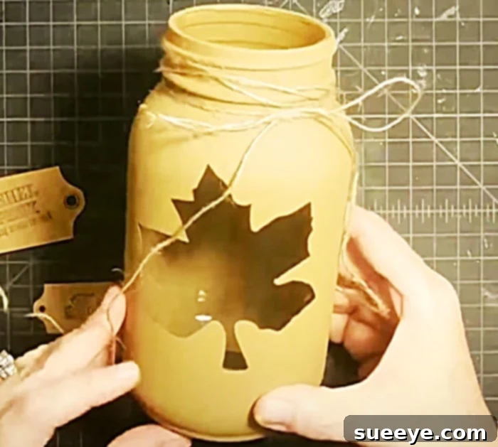 Crafting a Fall leaf mason jar candle holder, showing the painted jar with a leaf stencil for autumn DIY decor