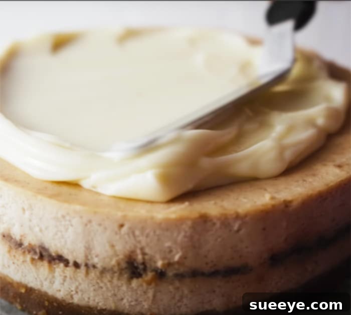 Ultimate Cinnamon Roll Cheesecake 3 How to glaze a Cinnamon Roll Cheesecake, showing the creamy topping being spread evenly