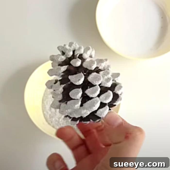 Frosted Forest Pinecone Ornaments 2 Flocked Pinecone Ornament glittering with snow-like effect on a work surface, demonstrating the glue and glitter application for DIY Christmas decor.