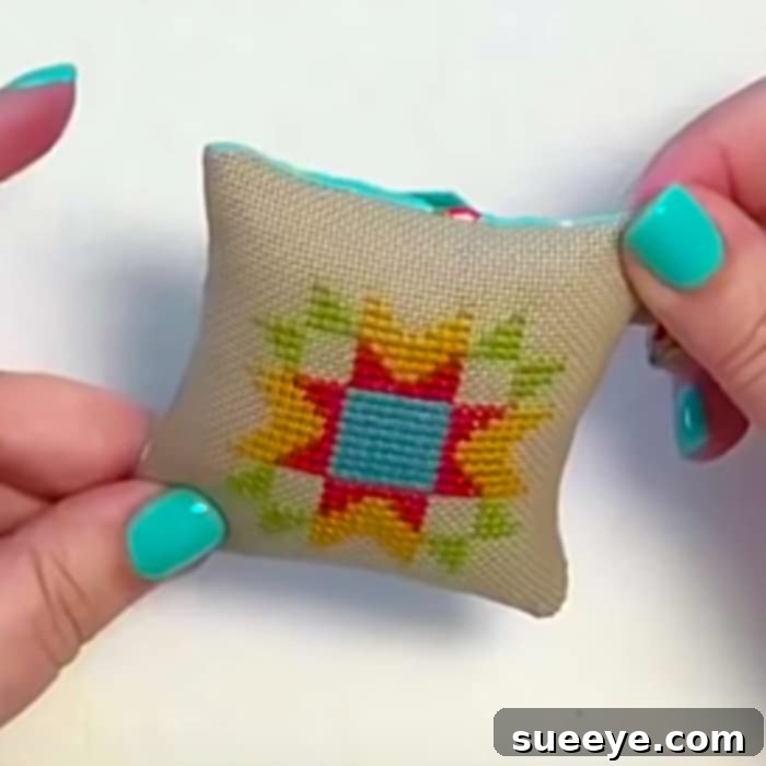 Close-up of a finished mini cross stitch pincushion, showcasing a beautiful handmade sewing accessory and gift idea.